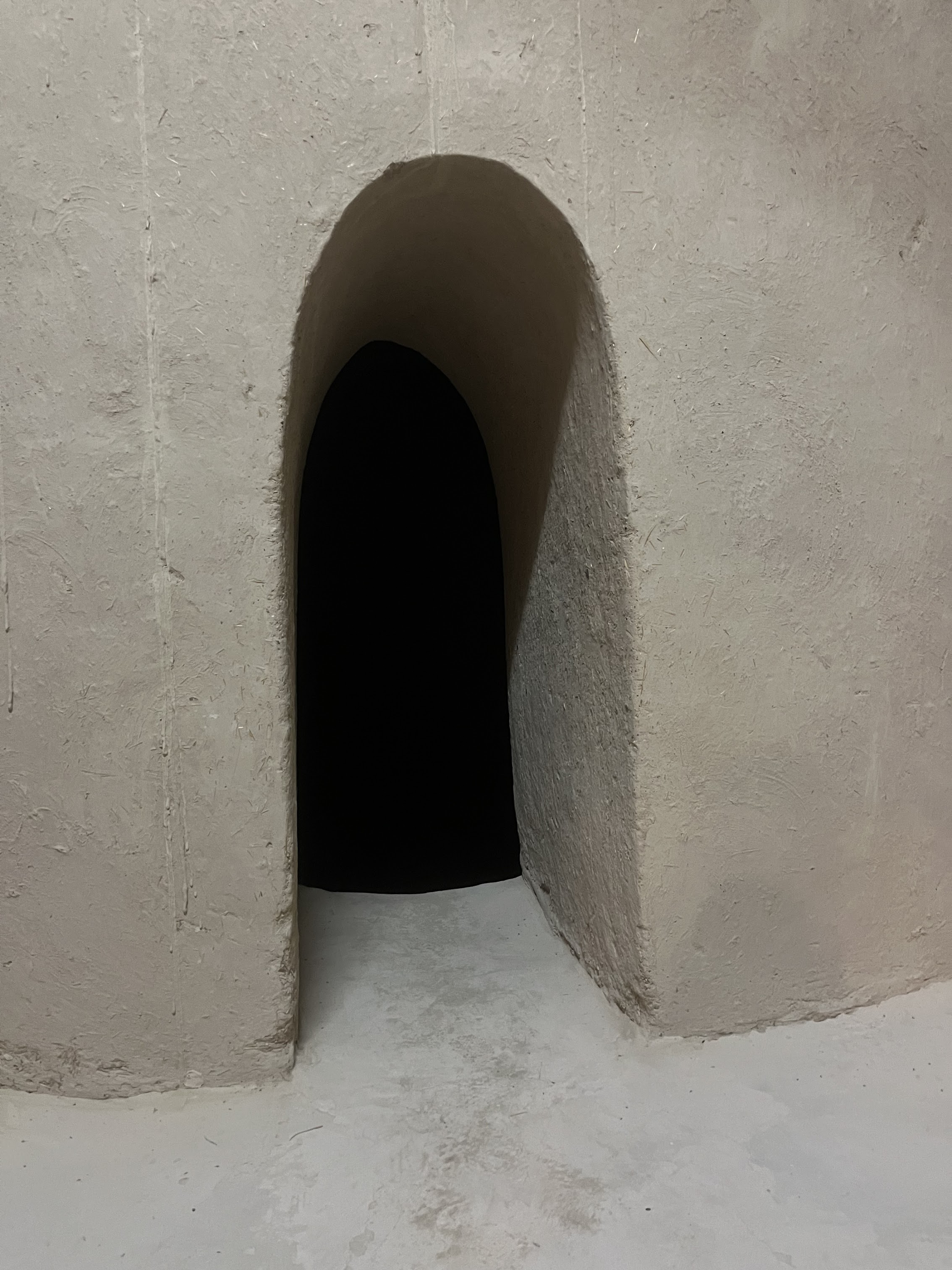 A narrow archway with a rounded top, set into an interior earthen wall, leads to dark unlit space beyond.