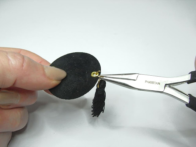 Closing the jump ring connecting the black tassel and the leather circle ith pliers