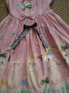 A green ribbon bow with long tails covered in lace and smaller ribbon bows at the tips lain upon the Marshmallow Bunny jumperskirt.