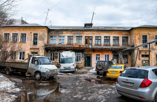 Припаркованные машины в лужах на фоне дом с ветхим балконом