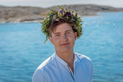 Porträttbild av Daniel Norberg framför havet, med midsommarkrans på huvudet.