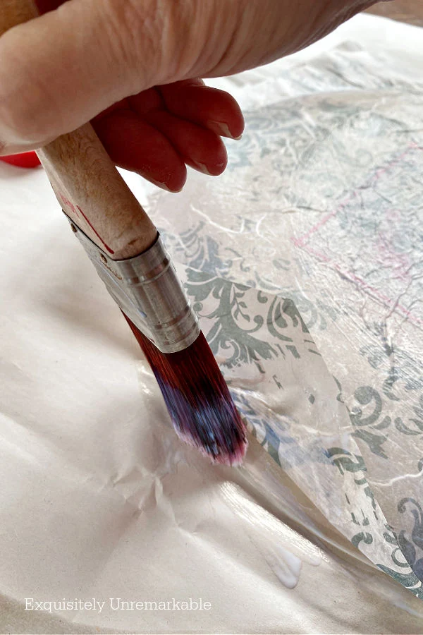 Brushing decoupage gel around edges of a glass dish and napkin