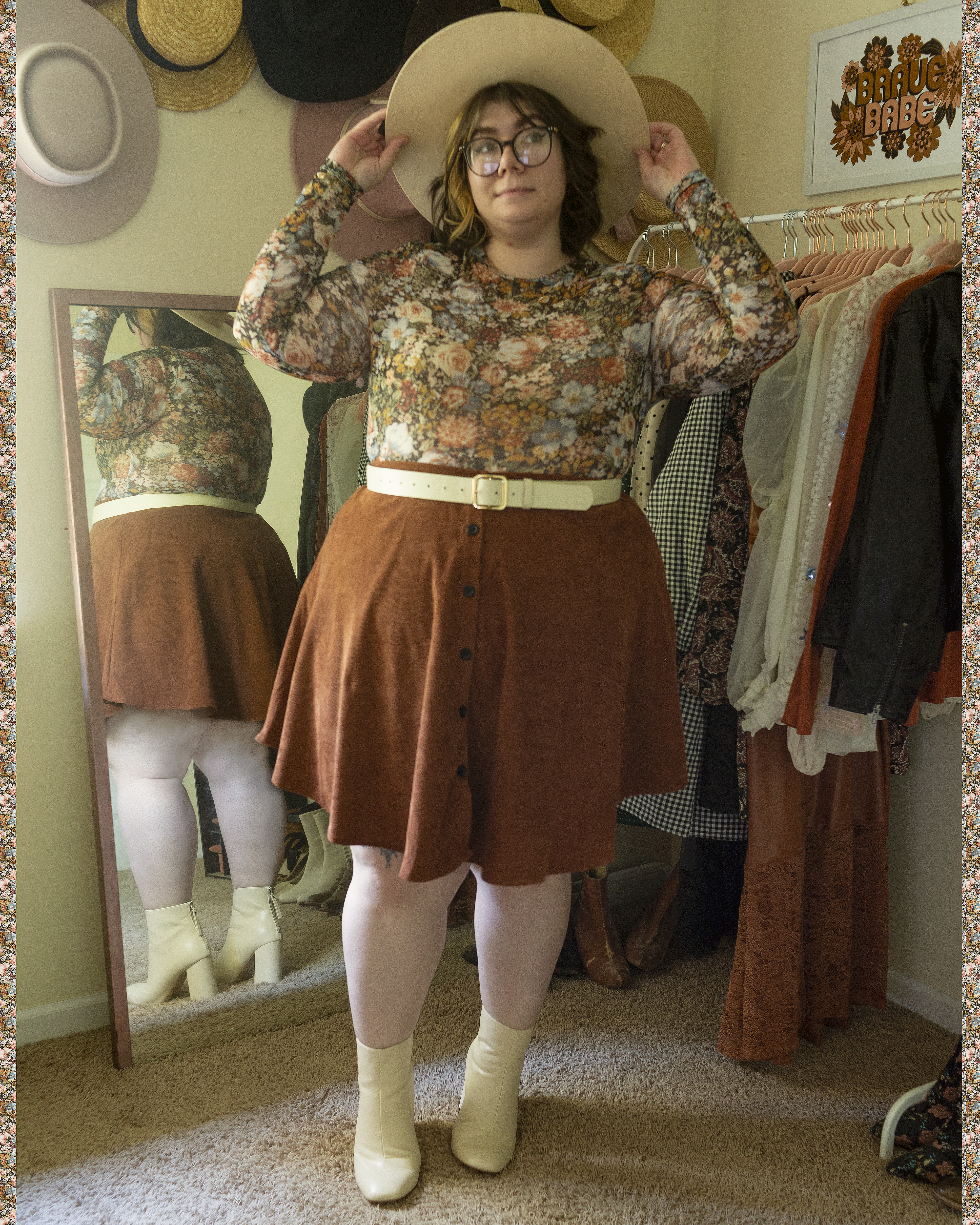 An outfit consisting of a beige wool wide brim boater hat, a mesh black with white, steel blue, burnt orange, pastel pink, mustard yellow, maroon and sage green floral print tucked into a brown corduroy button up midi A-line skirt and cream boots.