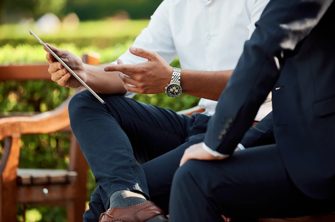 A person holding a tablet and point finger to it while sitting on the table in a park wearing watch photo