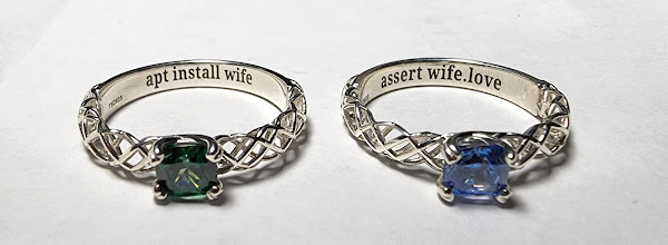 two rings on a white background; on the left, a silver ring with a green stone, with an inscription on the inside that says "apt install wife"; on the right, a silver ring with a blue stone, with an inscription on the inside that says "assert wife.love"
