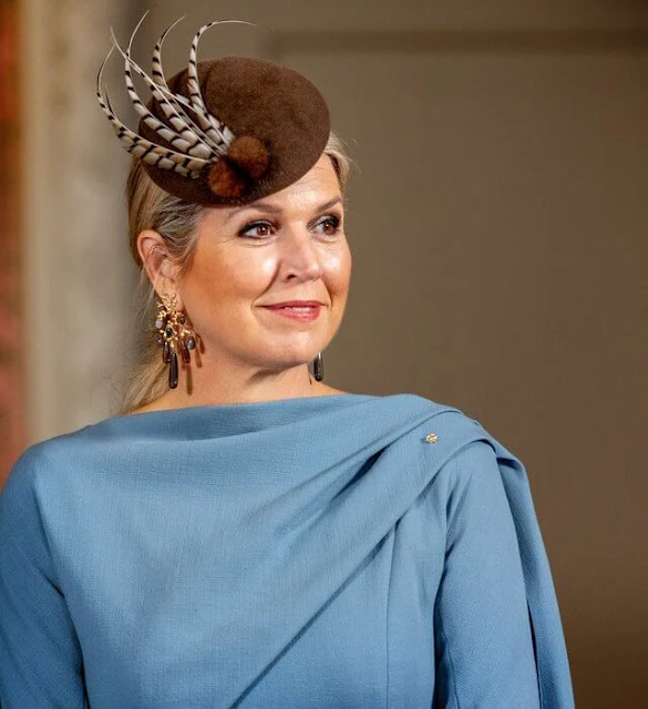 Queen Maxima wore a sky blue silk cape dress by Natan. She wore a wool camel coat. Ole Lynggaard gipsy earrings