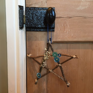 Wooden pentagram with dried flowers hanging from the wrought iron doorknob of a wooden door