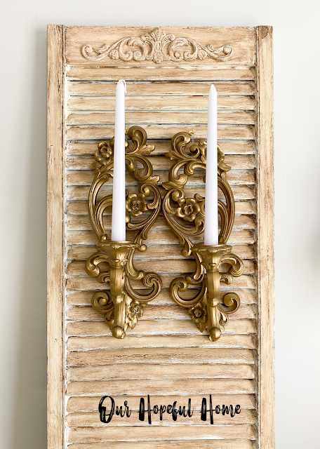 distressed vintage shutter with two gold candle sconces and white tapers