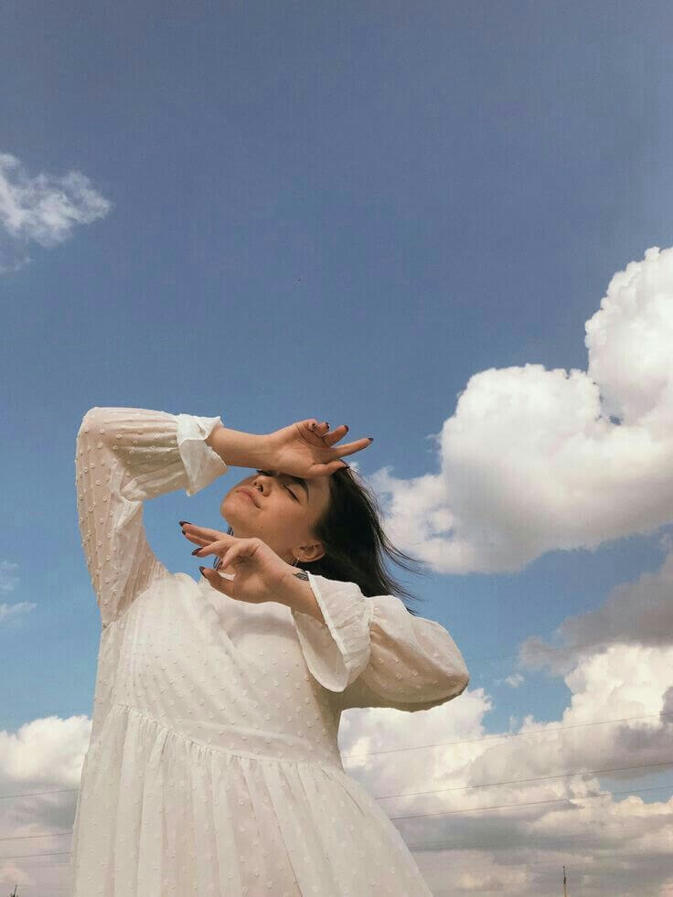 Foto aesthetic chica posando tapandose el rostro con el cielo y nubes de fondo