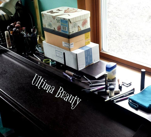 Various makeup and makeup brushes with a stack of shoe boxes on top of a closed upright piano