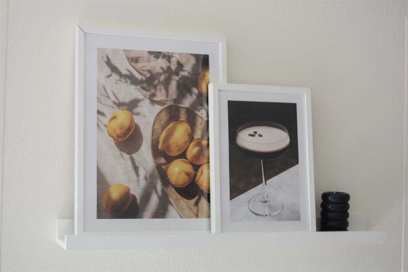 Twee Desenio posters in lijsten op een fotoplank. Poster met citroenen en poster van espresso martini.