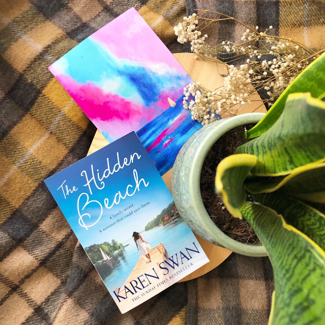 Cover of 'The Hidden Beach' by Karen Swan next to a print of a painting of a boat under a blue and pink sunset