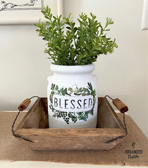 Photo of an upcycled crock with spray paint & decor transfer displayed in a barn wood basket.