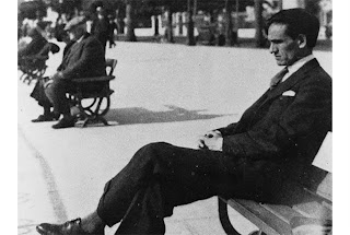 El poeta peruano César Vallejo sentado en una banca con las piernas cruzadas y la mirada y el rostro tristes