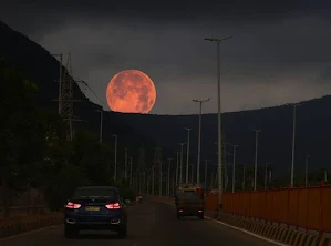 The Moon rises behind some low hills