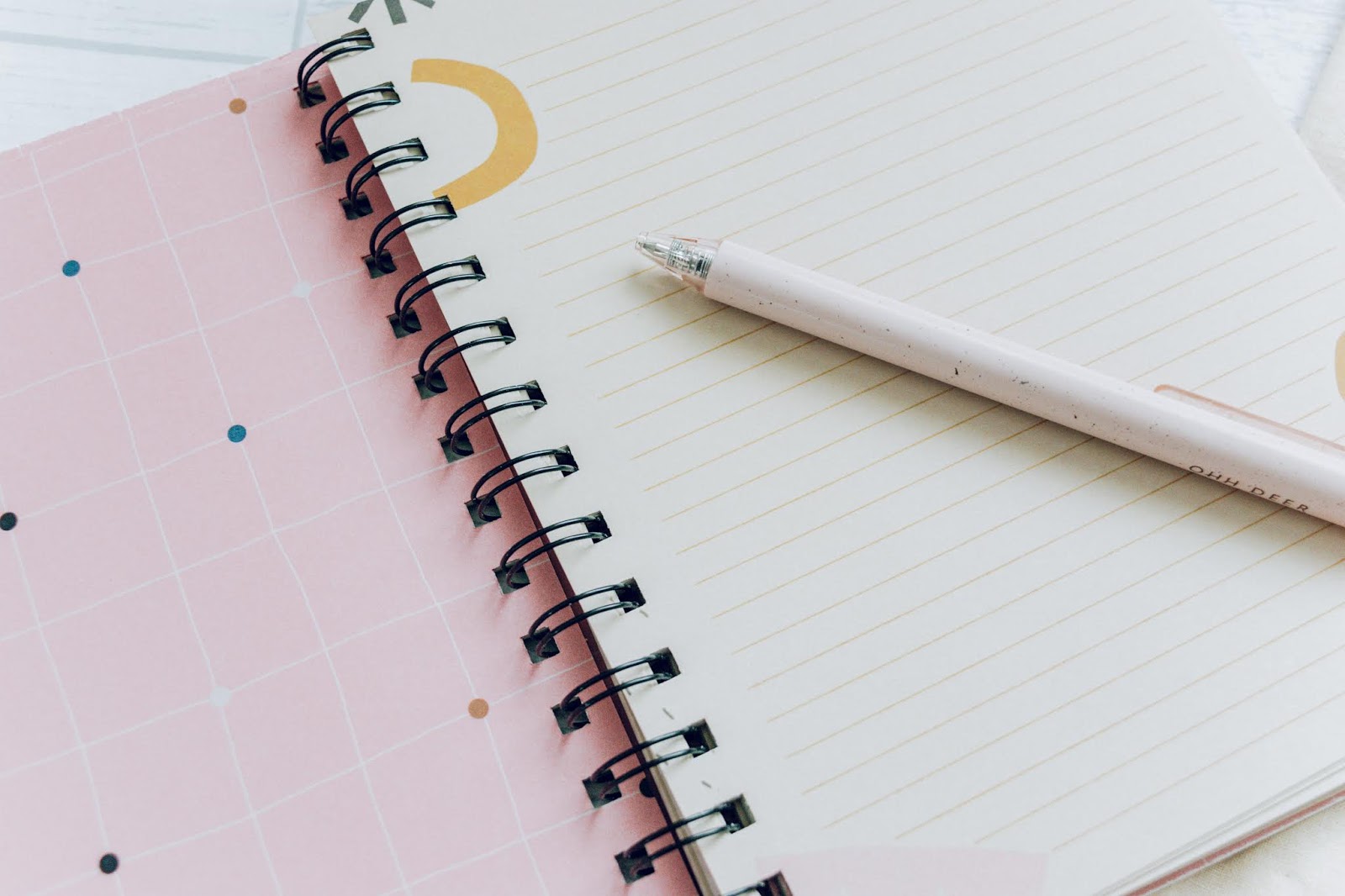 A spiral bound notebook with beige lined pages and geometric shapes around the edges.