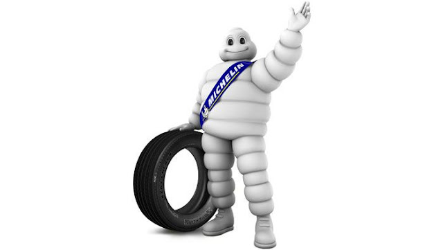 A 3-D cartoon of the Michelin Man, waving, and standing next to a tire.