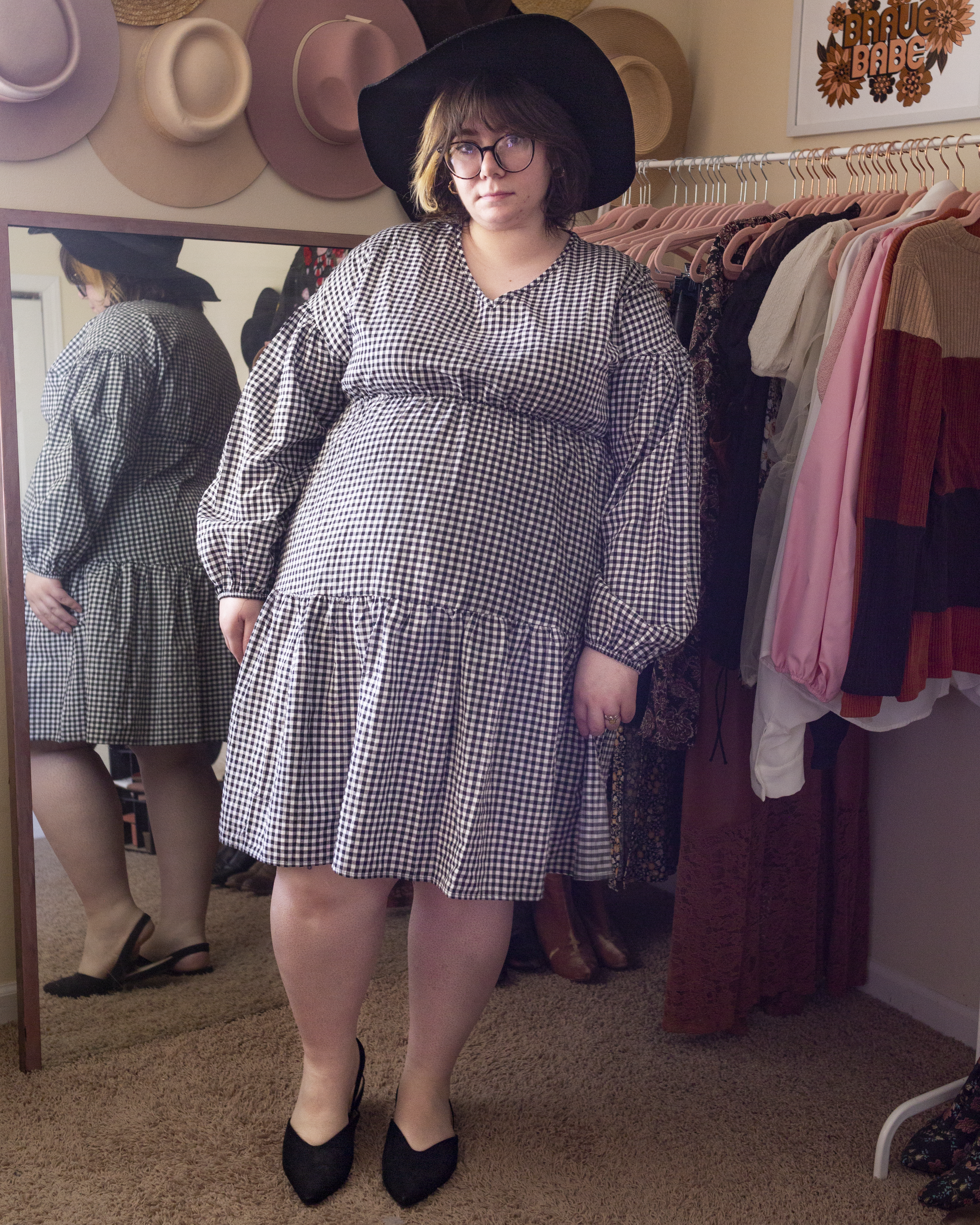 An outfit consisting of a black wide brim fedora, a black and white gingham long bishop sleeve dress and black slingback flats.