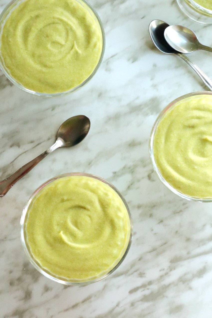 several cups of avocado mousse along with spoons seen from above