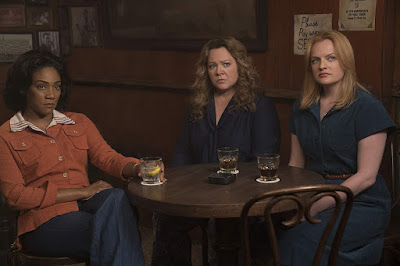 Movie still for "The Kitchen" (2019) featuring Tiffany Haddish, Melissa McCarthy, and Elisabeth Moss sitting at a table in a bar