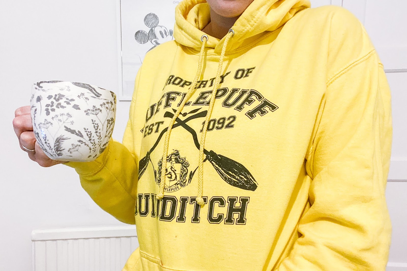 Girl wearing a yellow Hufflepuff hoodie holding a mug of tea.