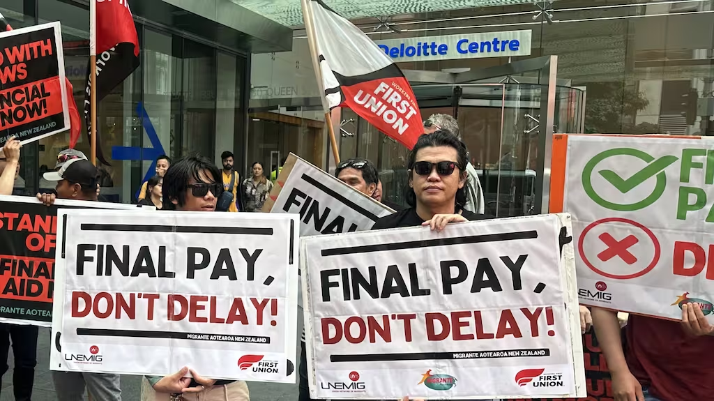 Hai người biểu tình cầm tấm biển có nội dung 'Thanh toán đi, đừng trì hoãn!' bên ngoài tòa nhà trung tâm Deloitte trụ sở tại Auckland.