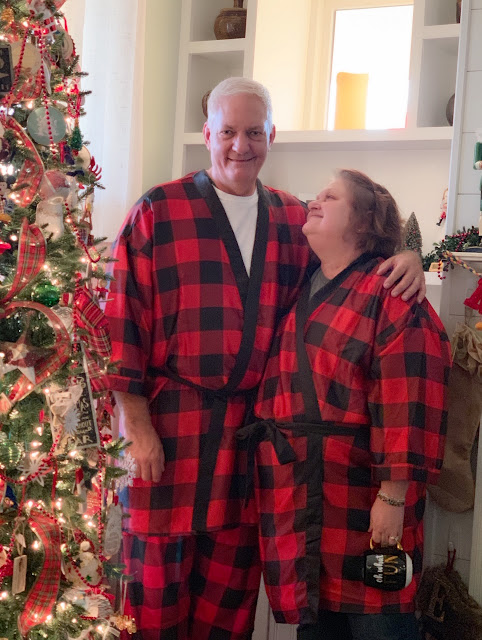 Decorated Christmas tree, with a woman looking adoringly at a man and wearing matching pajamas.