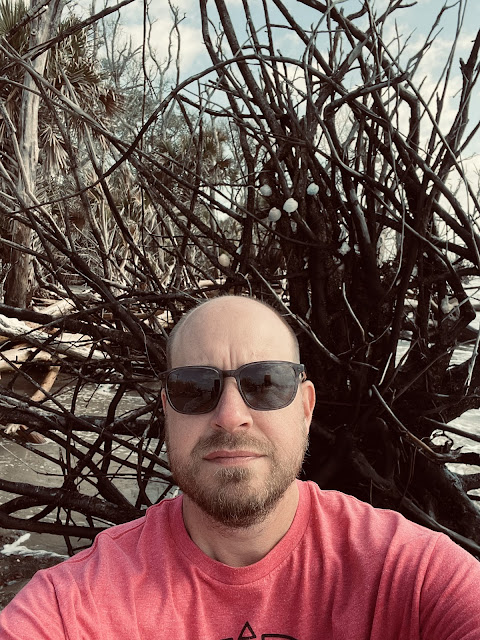 A selfie of dad on the forest beach in front of a tangle of branches.