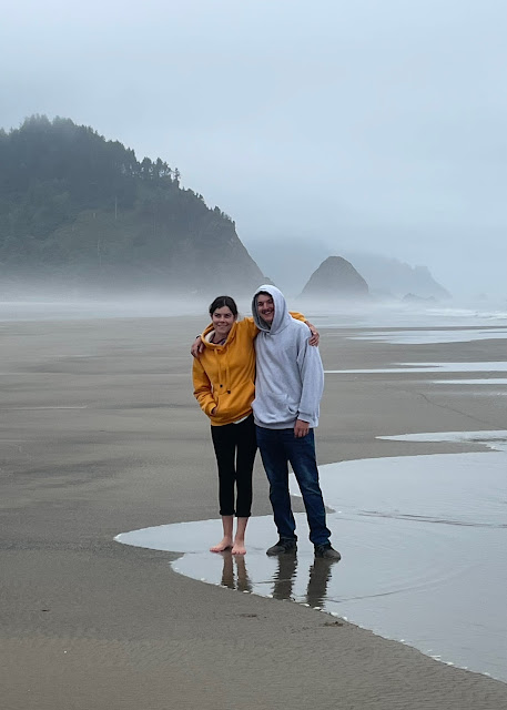 You and Andy standing on the beach, arms around each other. You are standing right on the edge of the tide, the sand is wet, and the sky is overcast. There is a fog building up behind you.