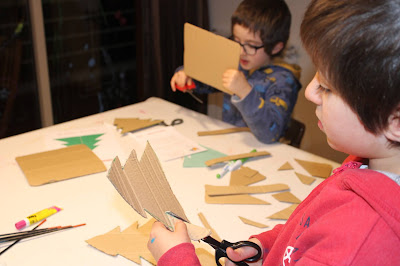 duas crianças a cortar o desenho de duas árvores de Natal em cartão