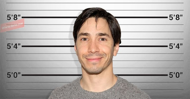 Justin Long posing in front of a height chart background