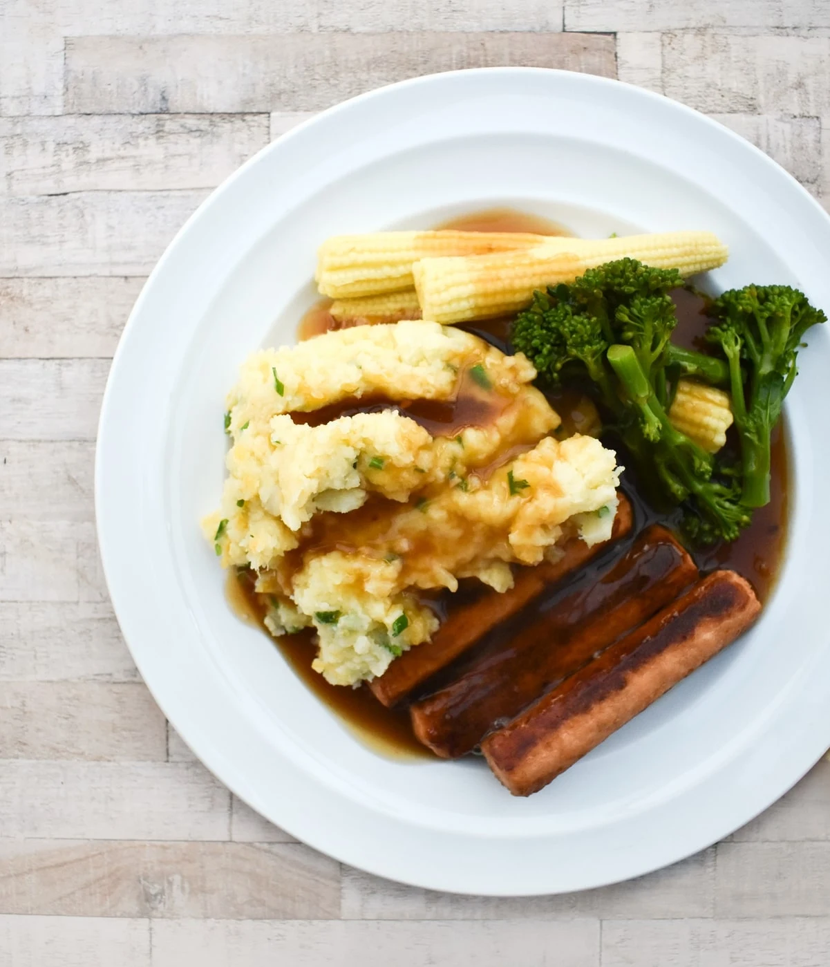 Sausages, veg, clapshot and gravy on a plate.