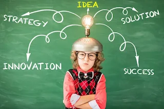 Gümüş bir kask giyen bir kişi, üzerinde bir ampul olan bir kaskla yeşil bir tebeşir tahtası önünde duruyor. Tahtada ‘strateji’, ‘inovasyon’, ‘fikir’, ‘çözüm’, ‘başarı’ kelimeleri ve bu kelimeleri birleştiren sarı oklar bulunmaktadır.