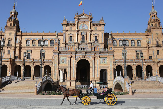 Edificio principal de la plaza de España de Sevilla con un coche de caballos con turistas pasando por delante.