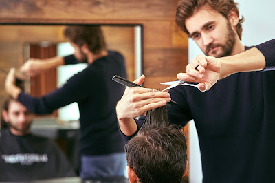 Pic of barber cutting man's hair with sharp scissors and comb reflected in mirror