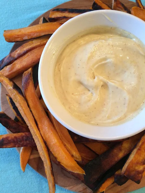 Creamy maple mustard dipping sauce in a ramekin surrounded by baked sweet potato fries.