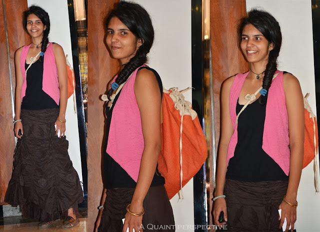 Black camisole with brown full length skirt, a bright pink waistcoat, and an orange jute bag.