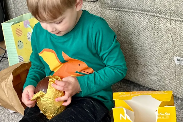 A boy ripping open the foil on a NOMO caramel Easter Egg