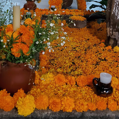 Marigolds. Lots of marigolds and their petals arranged and scattered around clay pots containing white candles and- even more marigolds.