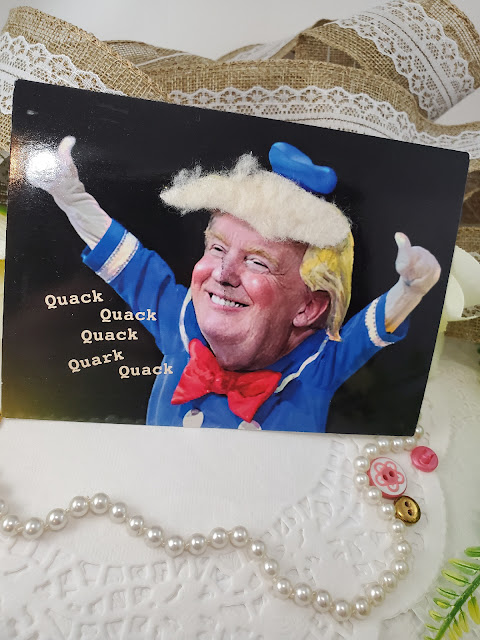 A postcard image of Donald Trump on Donald Duck's body. Text reads, "quack quack, quark, quark". The hair is fuzzy blonde cotton.