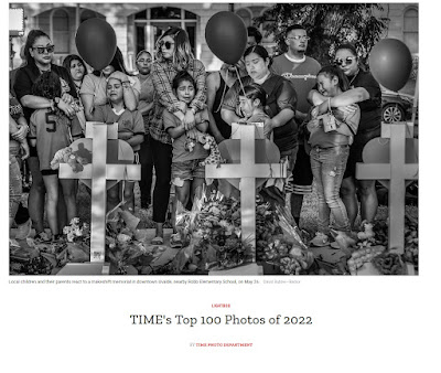 black and white photograph of Local children and their parents standing by a makeshift memorial with crosses in downtown Uvalde, nearby Robb Elementary School, on May 26 by David Butow