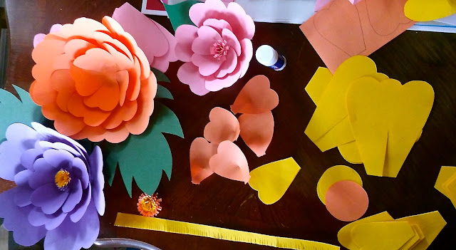 purple, orange, and yellow paper flowers on a table with flower pieces for assembly