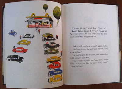 Rows of cars in a parking lot with red, gold, white and black McDonald's building in the background