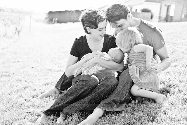 family sitting in grass with toddler and newborn