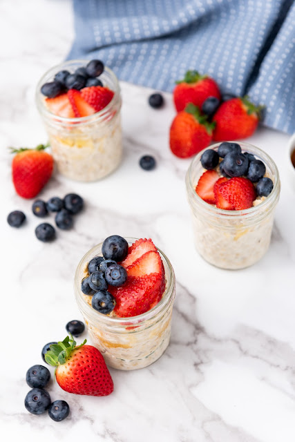 oats in jars with fresh fruit on top on a marble background.