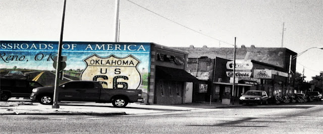 a selective color photo of the corner of US HWY 81 and US HWY 66 with a mural that says Crossroads of America painted on the side of a building in the small town of El Reno Oklahoma