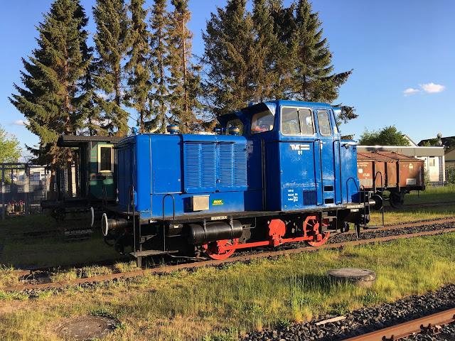 Die blaue Rangierlok und im Hintergrund ein Güterwaggon und ein grüner Personenwaggon.