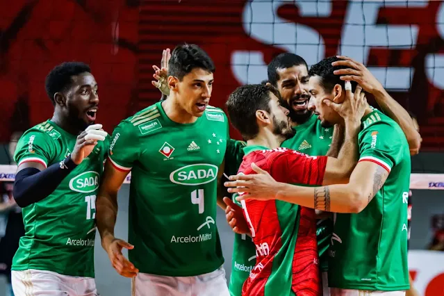 Jogadores do Cruzeiro comemoram um ponto se abraçando. Eles vestem o uniforme alternativo do clube na cor verde. O líbero usa uma camisa vermelha
