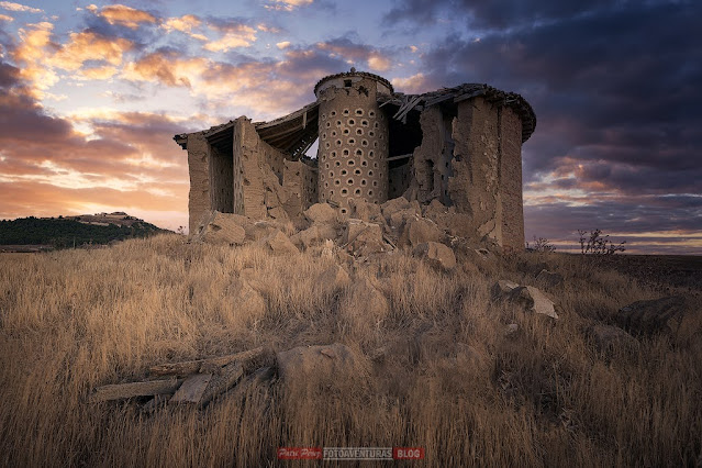 palomar de adobe abandonado con la mitad de la fachada en ruinas sobre un campo de hierba seca