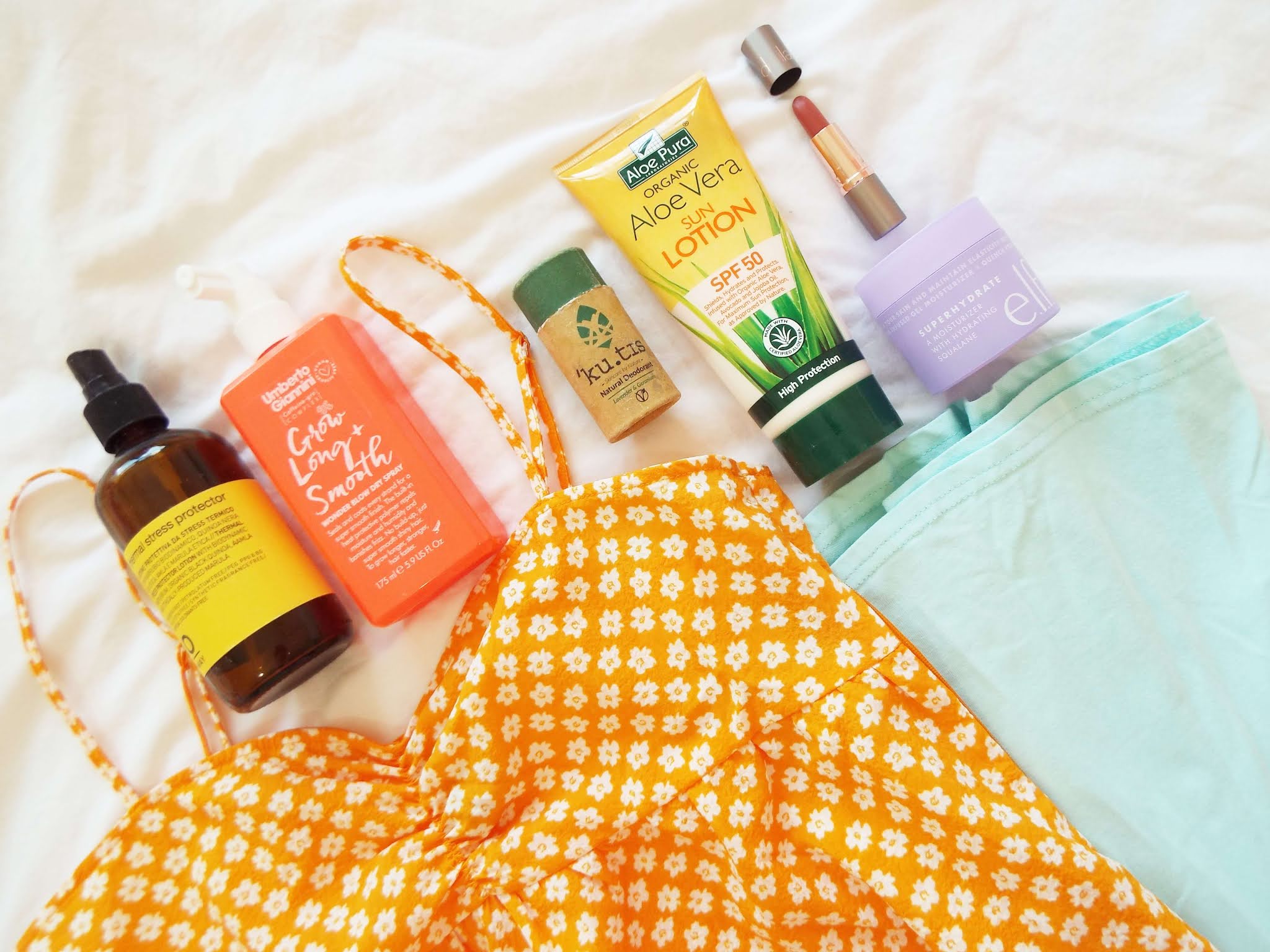 Warm toned flatlay of Summer beauty products and two, folded, Summer dresses, in floral orange and pastel green.